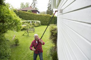 Mann maler fasade med forlengerskaft og rulle