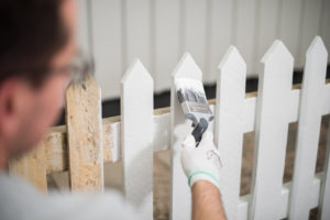 Bruker pensel til å stryke malingen jevnt utover gjerdet