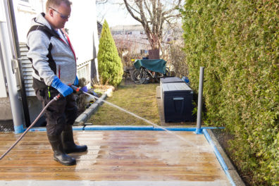 Mann spyler terrasse med hageslange